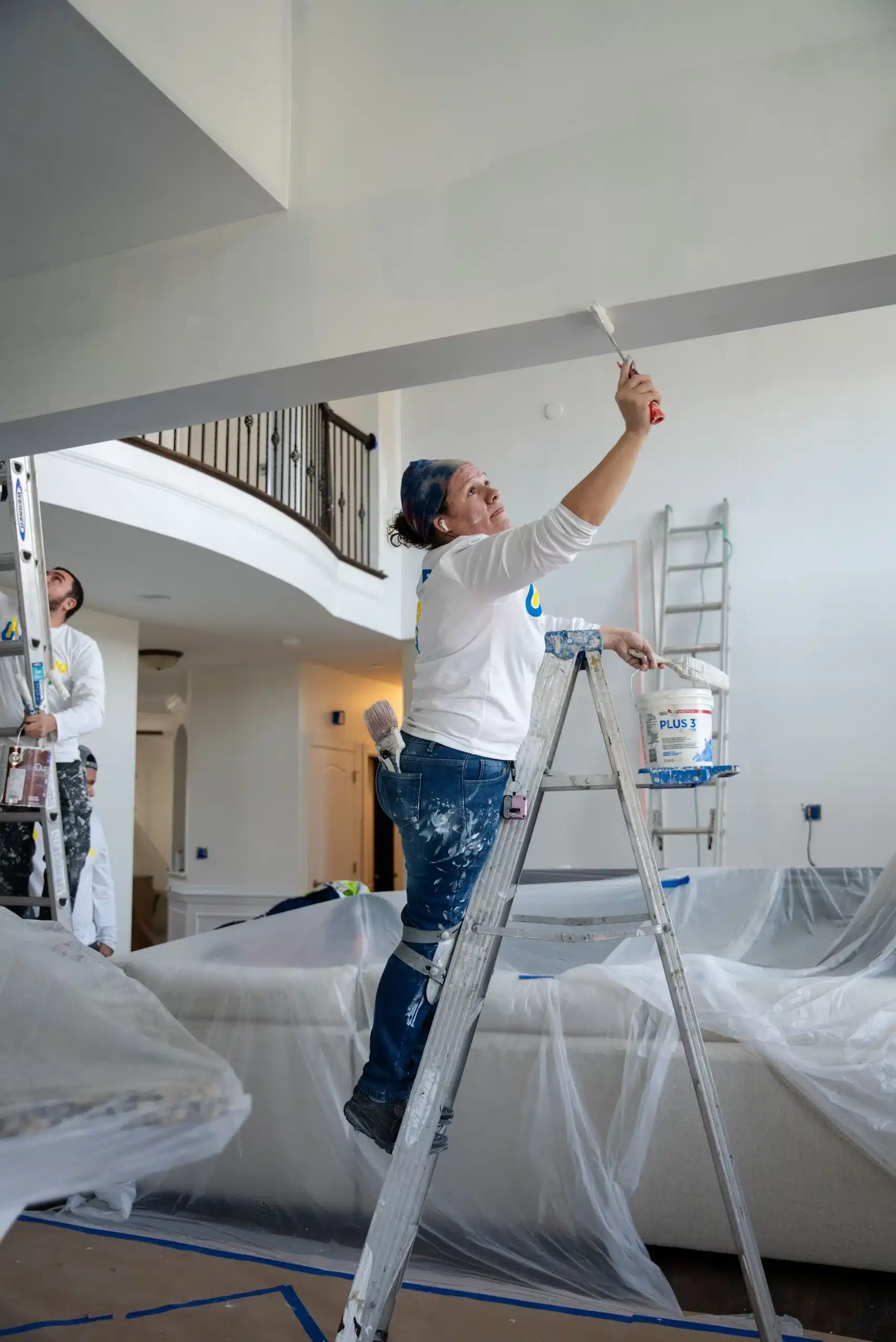 Expert Ceiling Painting Services for Residential and Commercial Spaces A professional female painter on a ladder carefully applies paint to a ceiling in a home.