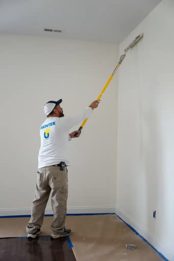 Efficient Interior Wall and Ceiling Painting by Professionals A professional painter uses an extension roller to efficiently paint a high wall in a residential room.