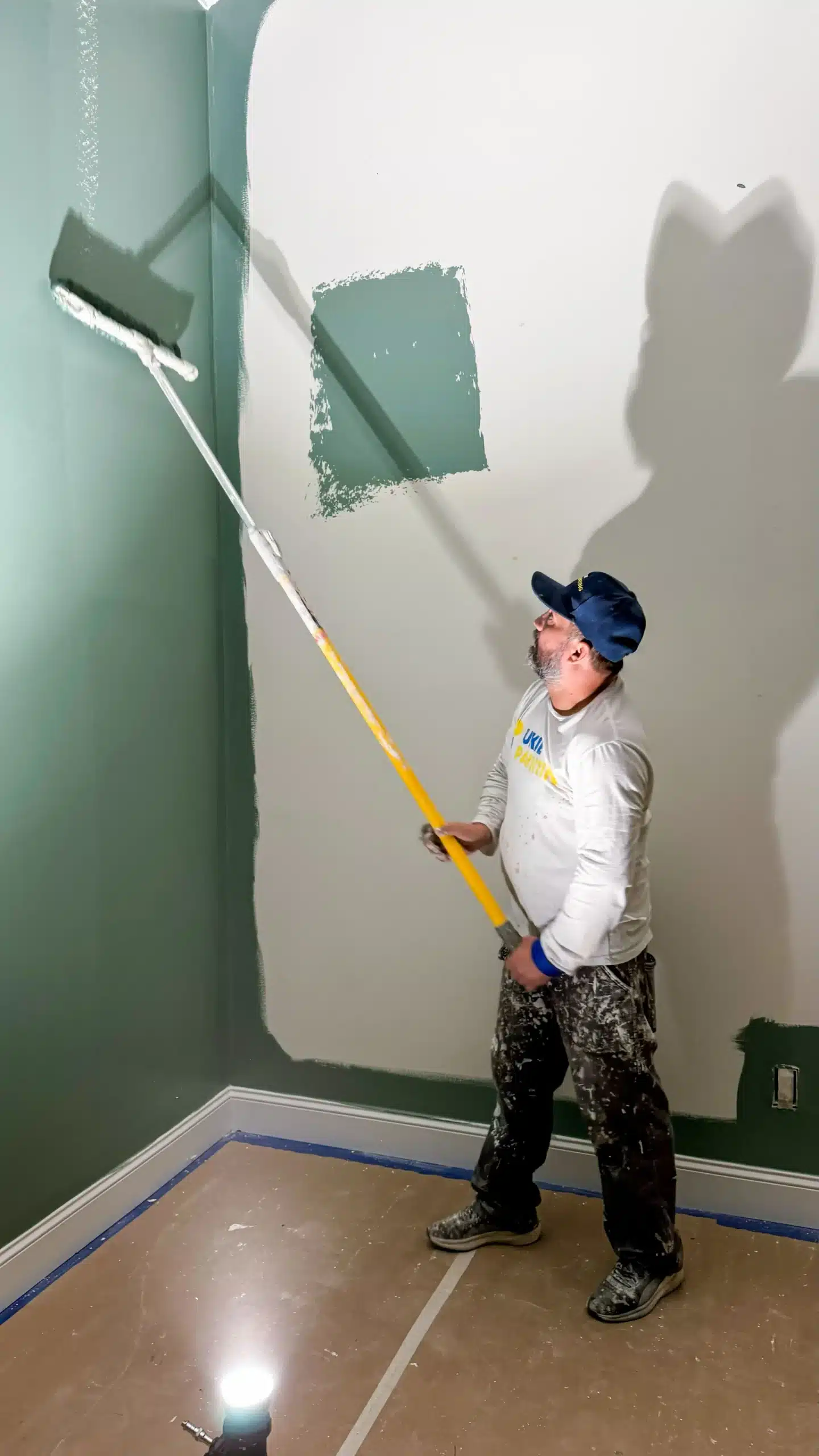 Interior Wall Painting Services with Quality Finish A professional painter using an extension roller to apply green paint to an interior wall.