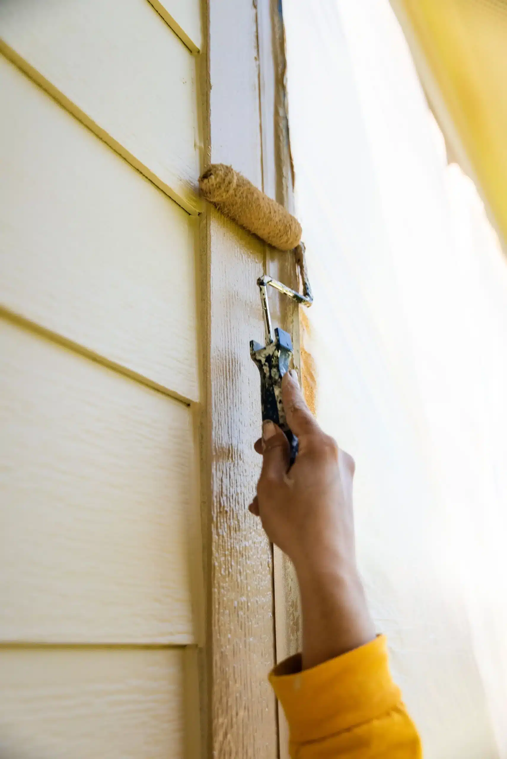 Expert Exterior Siding and Trim Painting Close up of a painter's hand using a roller to apply paint to exterior house siding.