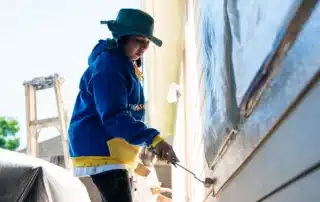 A painter carefully applying paint to exterior house trim with a small roller.