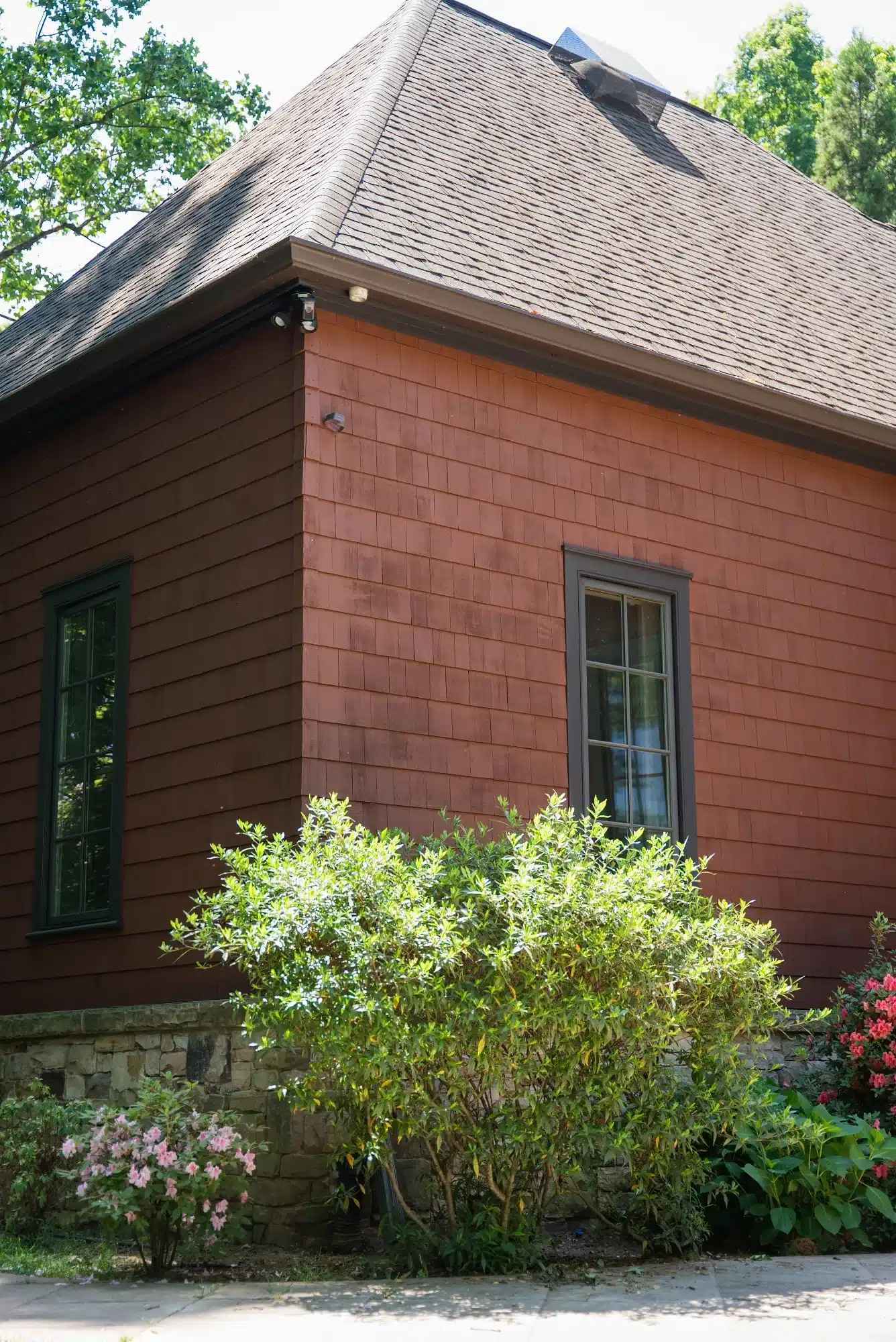 Rust Red Residential Exterior Rust red-painted residential exterior with dark green window frames, gray roof shingles, and stone foundation.